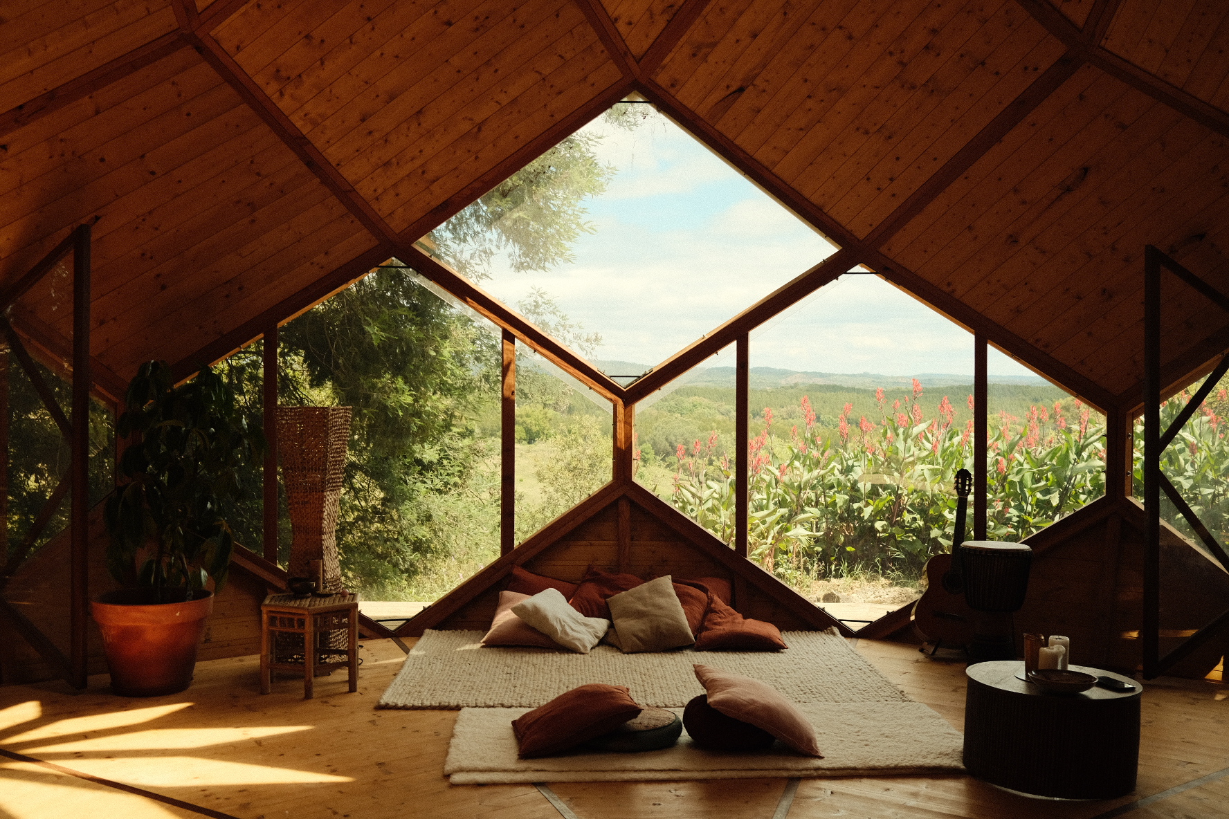 The warm wooden interior of a Zome with a large diamond window opening onto green hills